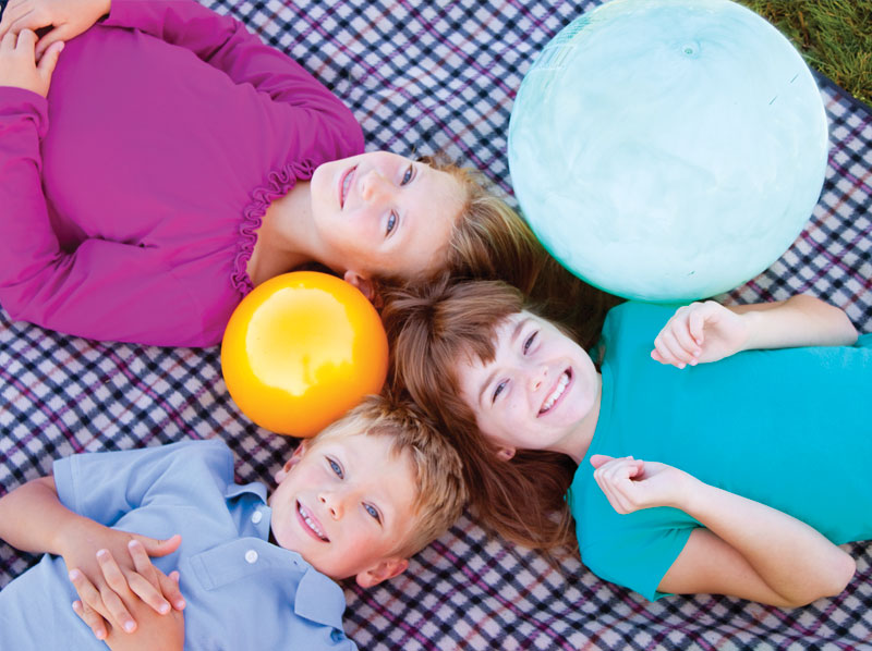 Two girls and a boy playing on a blanket with balls.